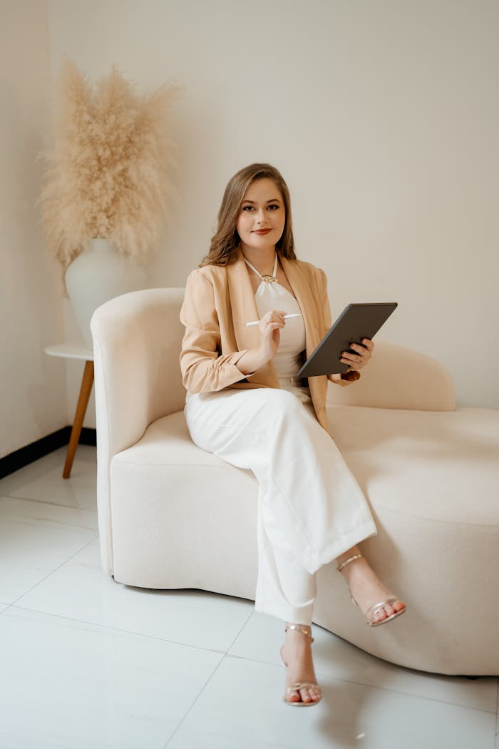 Confident woman in business attire browsing a tablet, seated in a stylish office setting.